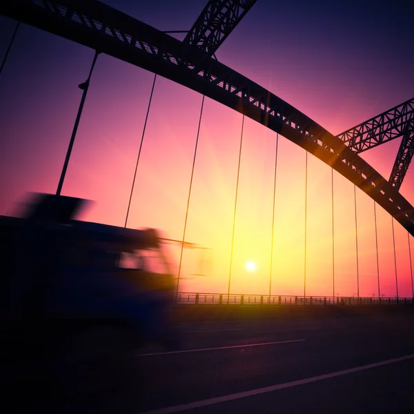 Вантажівка перевищує міст під час заходу сонця, розмивання руху . — стокове фото