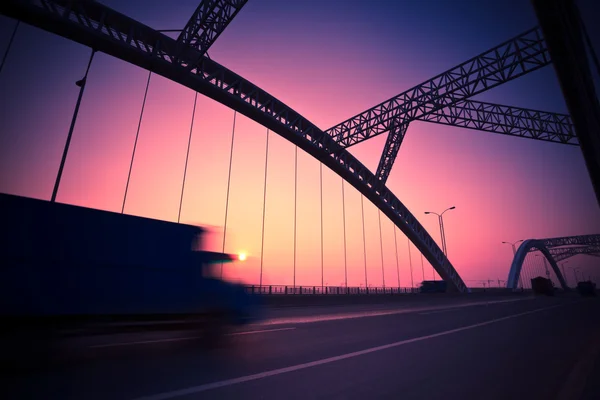 Lastbil fortkörning genom en bro vid solnedgången, rörelse oskärpa. — Stockfoto