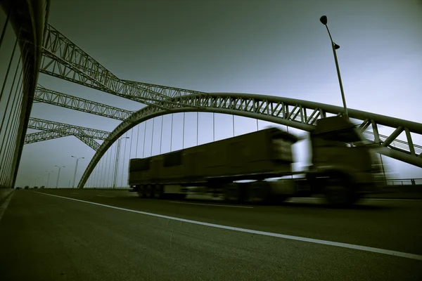 Vrachtwagen versnellen via een brug op zonsondergang, motion blur. — Stockfoto
