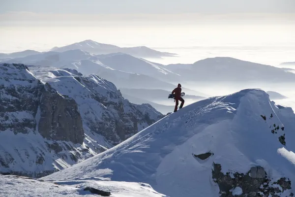 Mann erklimmt Gipfel mit Snowboard lizenzfreie Stockbilder