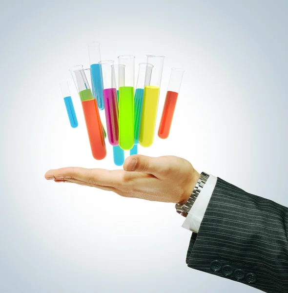 Різні лабораторні скляні посуд з кольоровою рідиною на руці бізнесмена — стокове фото