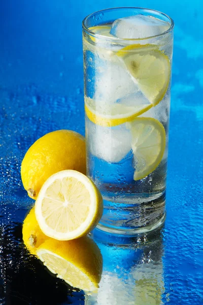 Стакан лимонной ледяной воды на голубом фоне — стоковое фото