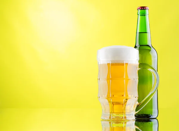 Caneca de cerveja e garrafas no fundo amarelo — Fotografia de Stock