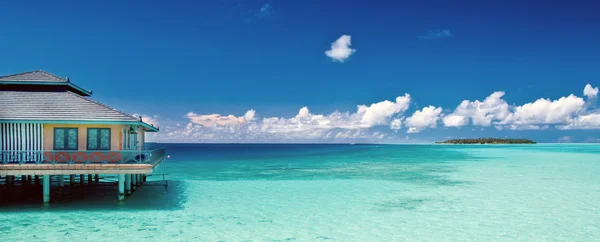 Пляжная панорама с водяной хижиной и далеким островом на Мальдивах — стоковое фото