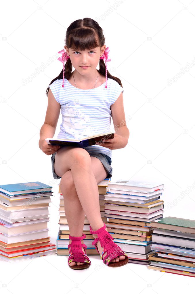 Schoolgirl sitting on the heap of books and reading one of them