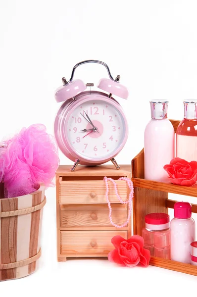 Reloj despertador y una gran cantidad de accesorios de cuidado del cuerpo de color rosa aislados en blanco — Foto de Stock