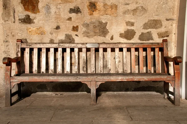 Деревянная скамейка с памятной табличкой напротив каменной стены — стоковое фото