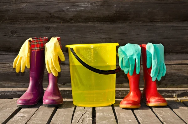 Bucket, rubber gloves and two pairs of rubber boots at wooden veranda