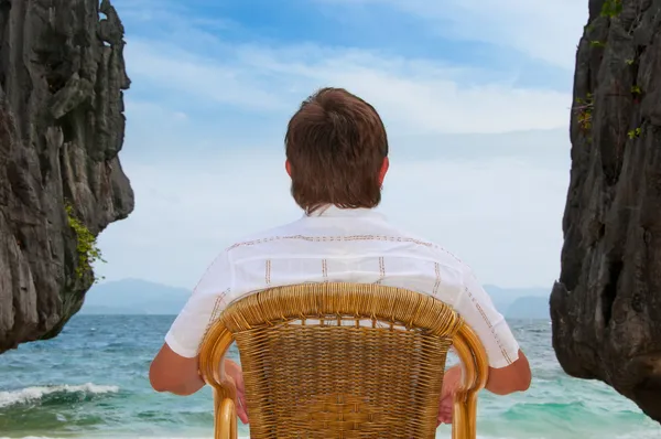 stock image Meditating man sitting at the beach between rocks looking at the sea