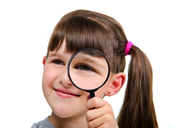 Beautiful little girl looking through a magnifying glass — Stock Photo, Image