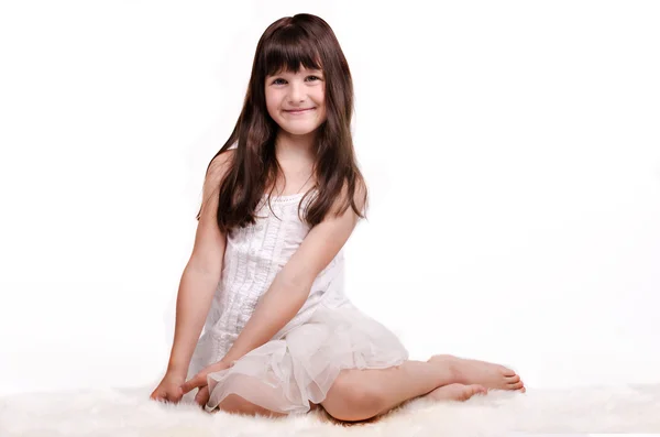 Chica sonriente en vestido blanco sentado en la alfombra blanca — Foto de Stock