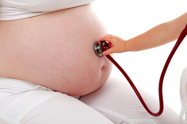 Kinderhand mit Stethoskop auf Schwangerschaftsbauch — Stockfoto