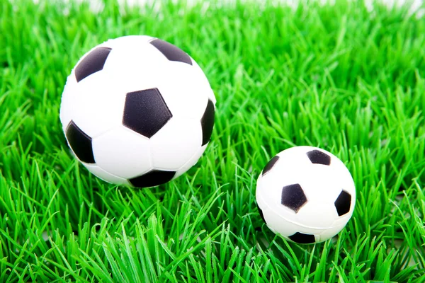 Una pelota de fútbol grande y una pequeña sobre hierba de plástico —  Fotos de Stock