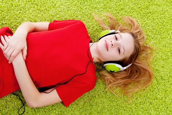 Girl is listening to music with headphones on green carpet — Stock Photo, Image