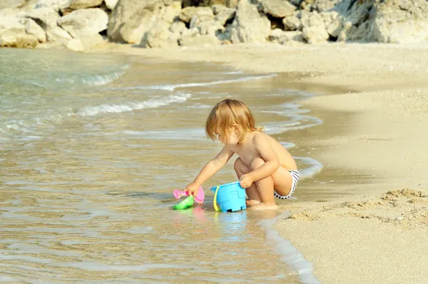 Happy toddler girl playing with her bucket at the beach — Stock Photo, Image
