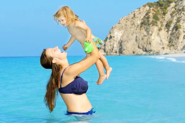 Unga och lyckliga barn flicka som leker med sin mamma på stranden — Stockfoto