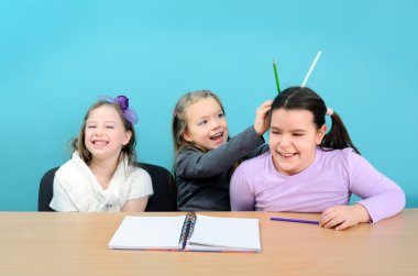 Three happy girls making jokes during class in school clipart