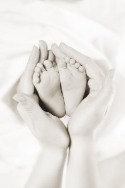 Mother holds baby feet in her hands clipart