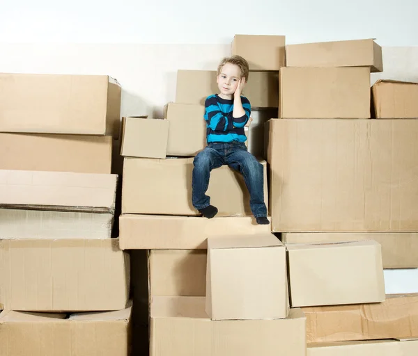 Dítě sedí na vrcholu zásobníku zabalené krabice. — Stock fotografie