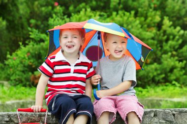 Two funny kids friends sitting under umbrella outdoor. Summer clipart