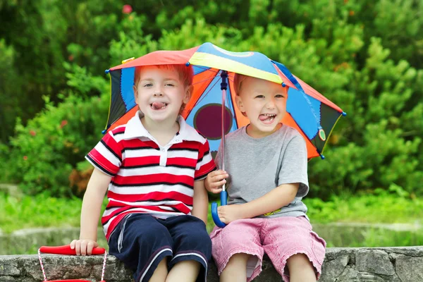 Two funny kids friends sitting under umbrella outdoor. Summer — Stock Photo, Image