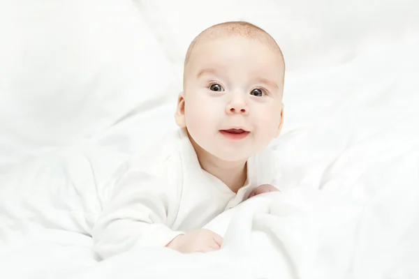 Glad aktiva barnet ligger på mage över vit säng. tre månaders — Stockfoto