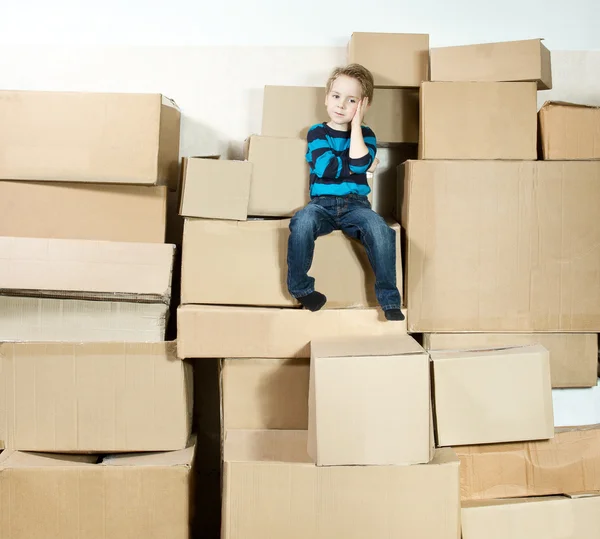 Child sitting on the top of heap of carton packed boxes. — Stock Photo, Image