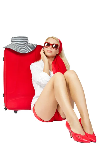 Красивая женщина сидит рядом с красным чемоданом и разговаривает по телефону — стоковое фото