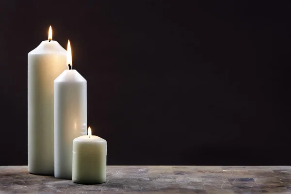 Drie kaarsen tegen donkere achtergrond Stockafbeelding
