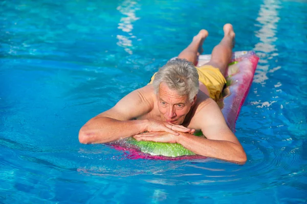 Літній чоловік плаває на повітряному матраці — стокове фото