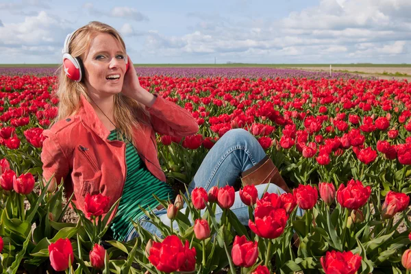 Dutch blond girl with headphones in field with tulips — Stock Photo, Image
