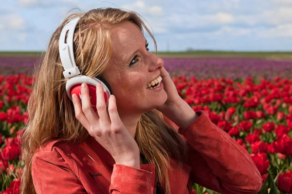 Chica rubia holandesa con auriculares en el campo con tulipanes — Foto de Stock