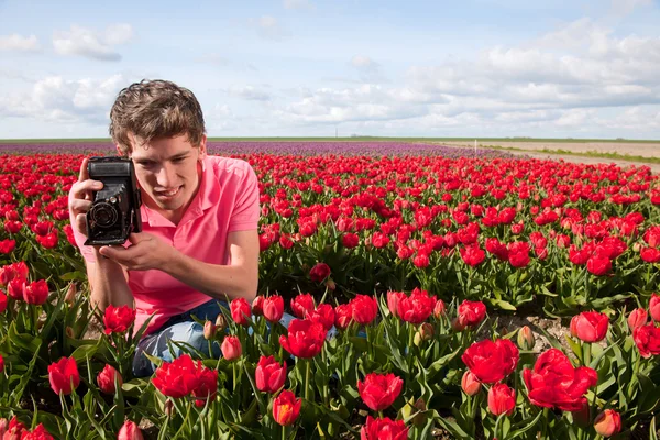 Yong hombre con cámara de fotos de edad en el campo con tulipanes —  Fotos de Stock
