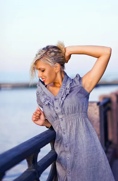 Blonde vrouw in grijze jurk op een kade. — Stockfoto