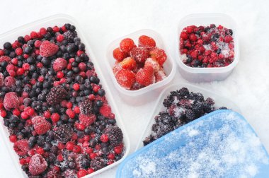 Plastic containers of frozen mixed berries in snow - red currant, cranberry clipart