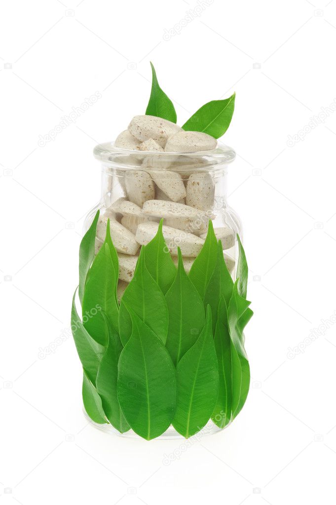 Herbal supplement pills and fresh leaves in glass – alternative medicine concept