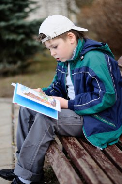 bir çocuk bir parkta bankta bir kitap okur