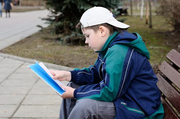 Un niño lee un libro en un banco del parque — Foto de Stock