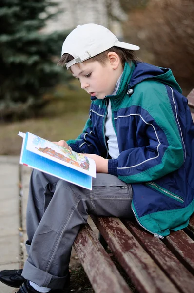 一个男孩在公园的长椅上读书 — 图库照片