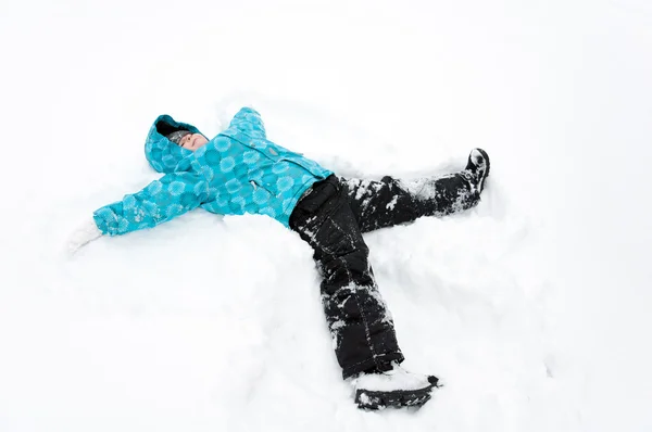 Мальчик в синей куртке лежит в снегу — стоковое фото