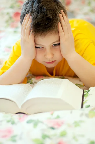一个男孩读一本书躺在床上 — 图库照片