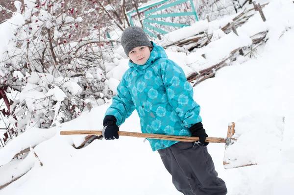 En pojke med en trä spade för snöröjning — Stockfoto