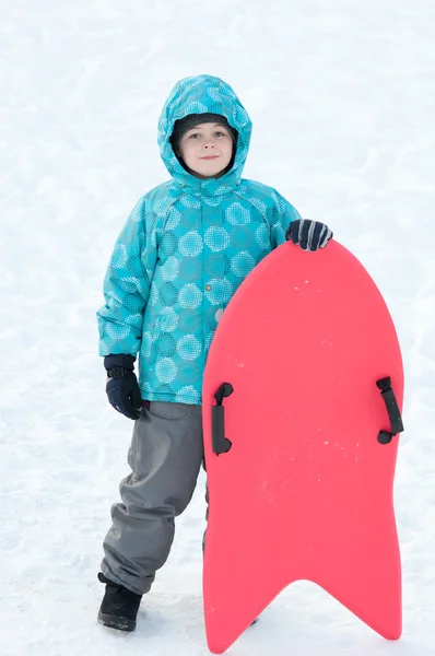 O rapaz com trenós vermelhos no inverno — Fotografia de Stock