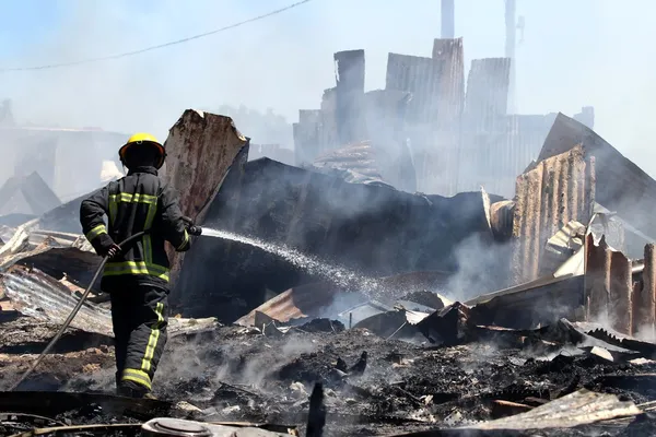 Feuerwehrmann schlaucht Überreste eines Barackenhauses Stockbild