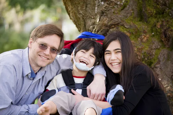 Handikappade pojken i wheelcahir omgiven av far och syster — Stockfoto
