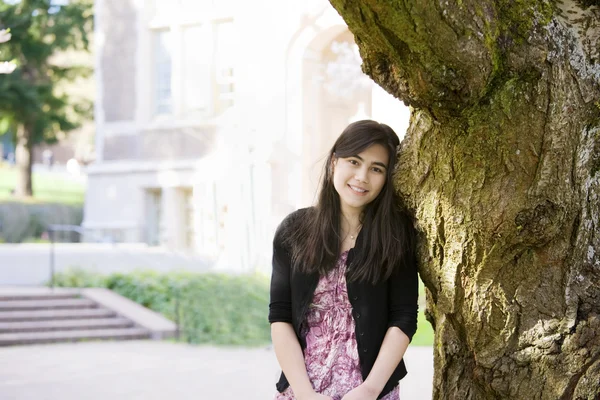Adolescente encostada contra tronco de árvore grande, sorrindo — Fotografia de Stock