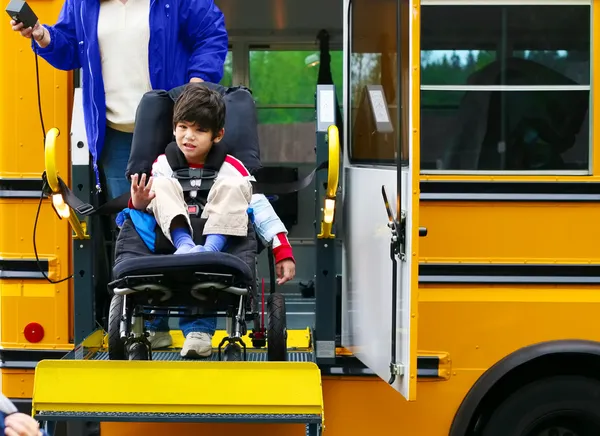 Niño de cinco años discapacitado usando un elevador de autobús para su silla de ruedas Imagen de archivo
