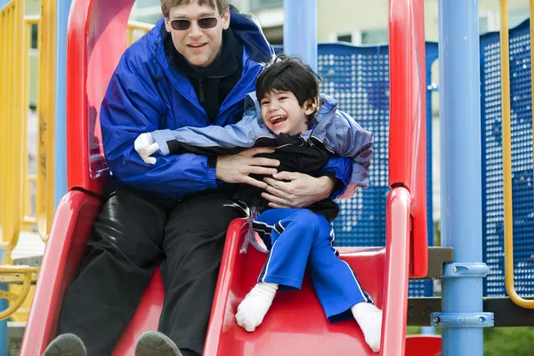 Baba Engelli oğlum serebral palsi hastası ile slayt aşağı gidiyor — Stok fotoğraf