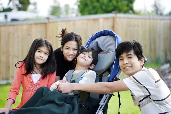 Drei Kinder umgeben ein kleines behindertes Kind im Rollstuhl — Stockfoto
