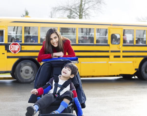 Sorella maggiore con fratello disabile in sedia a rotelle con scuolabus — Foto Stock